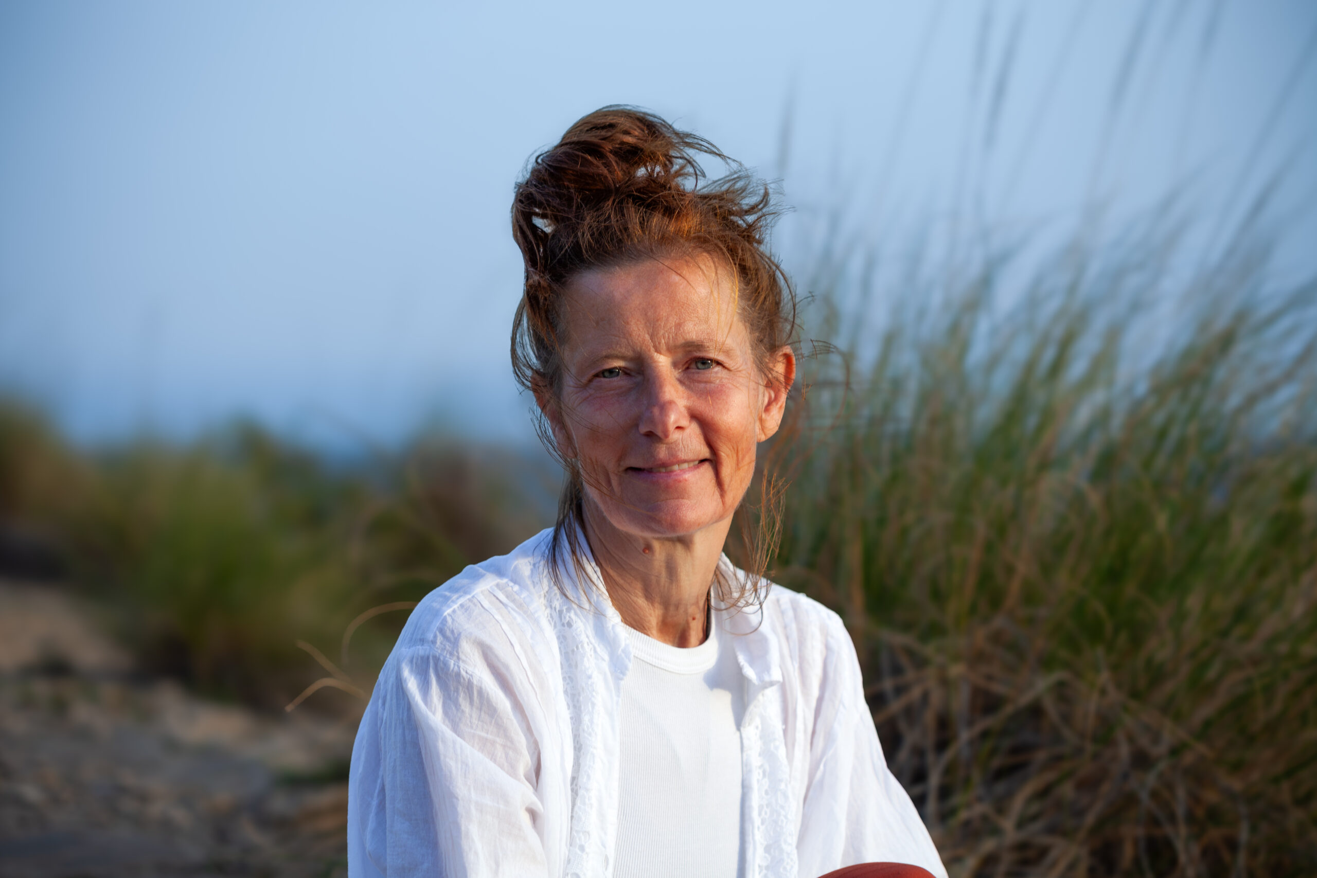 woman sitting between space of long grass at cliff in spain at sunset